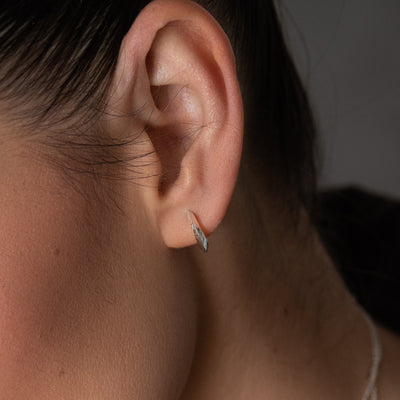 Made in Ireland, the Sterling Silver Torc Mini Detailed Hoop Earrings showcase a contemporary iteration of the Bronze Age 'Torc' neck collars. The earrings have a slightly curved shape that gracefully contours around the earlobe, while engraved with a Celtic motif design that beautifully reflects light.
