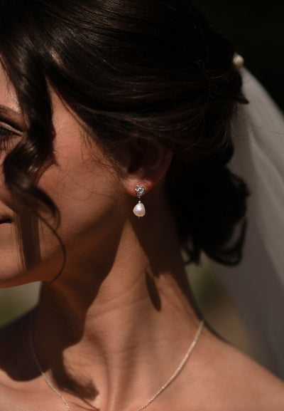 Close-up of a woman wearing silver pearl drop earrings with a veil. Simple bridal jewellery made in Ireland.