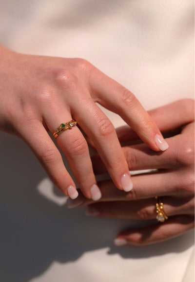 Close-up of a hand wearing a Tourmaline gold twig ring with a green gemstone on a neutral background